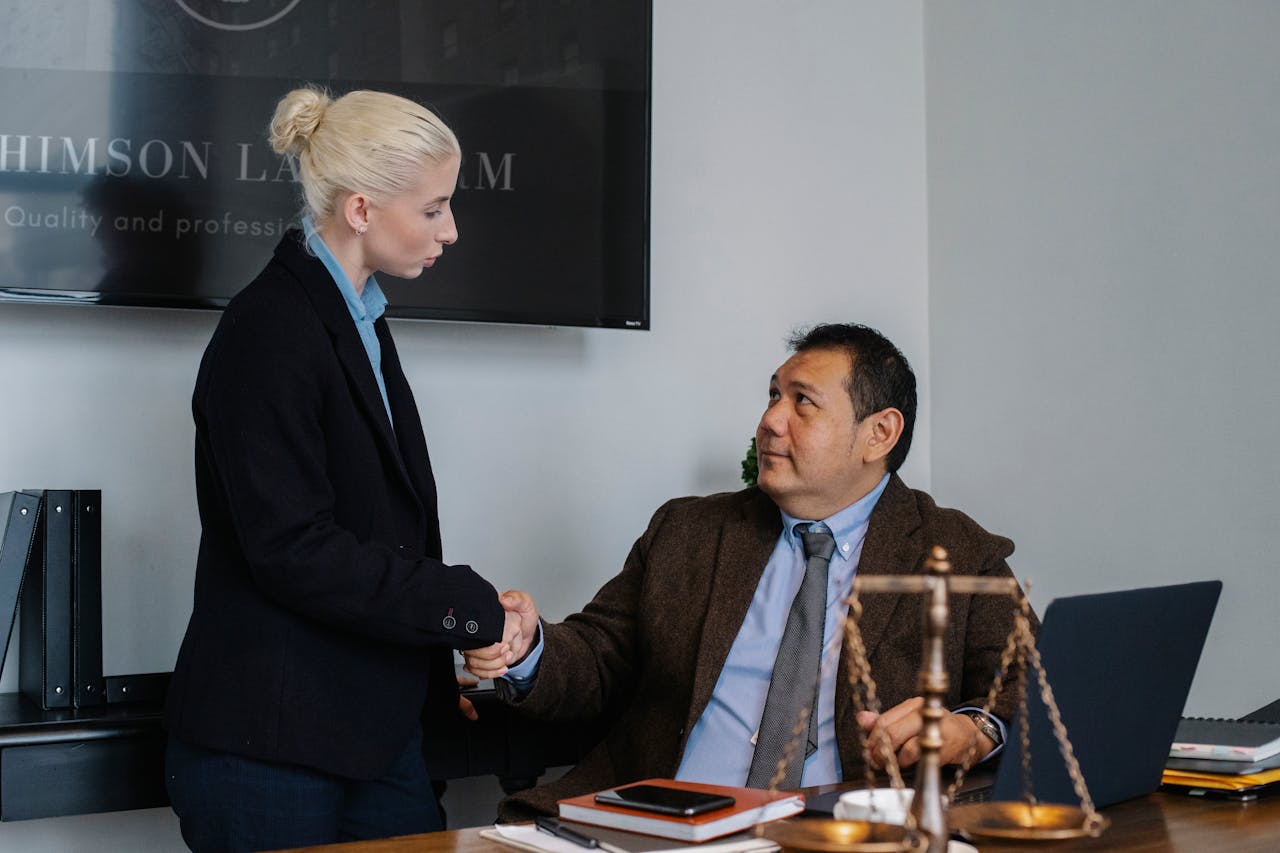 A male and female professional shaking hands in a law office environment.